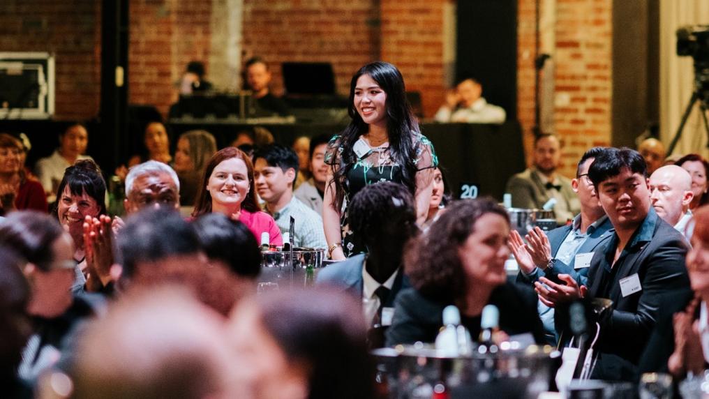 A large, warm, vibrant room full of people seated at tables and smiling