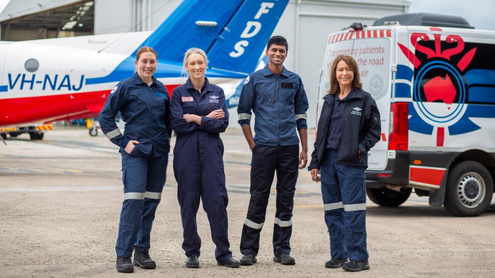 Paramedics in uniform pose with a small plane and ambulance