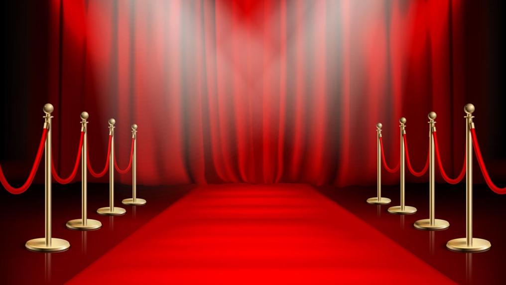 A red carpet surrounded by bright lights leading to a red curtain.