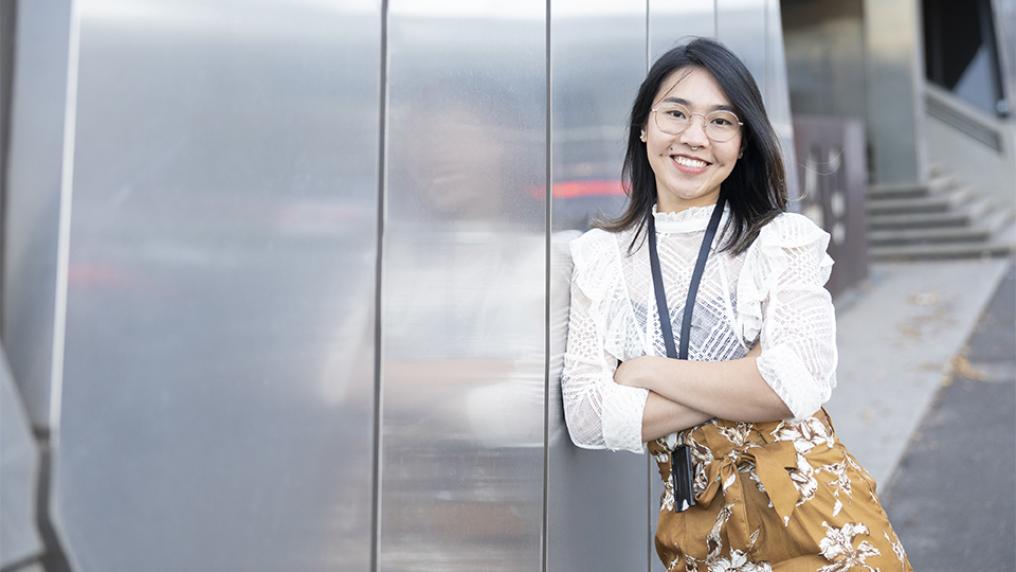 Student in a white shirt and yellow trousers leans against a reflective wall.