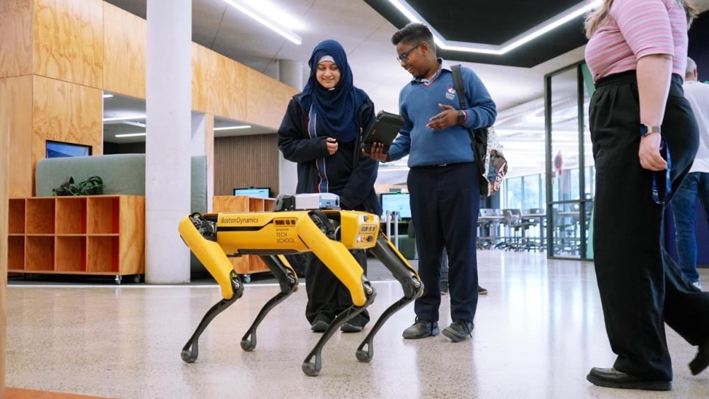 Students controlling a robotic dog using a handheld controller.