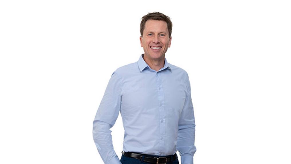 A middle aged man in professional dress smiles at the camera