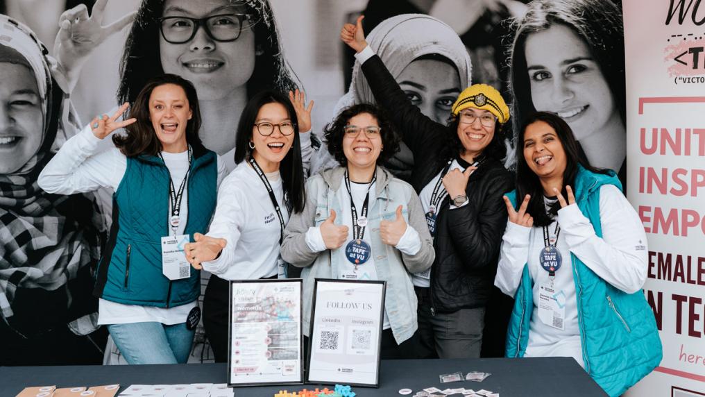 Five women standing at a VU Open Day stall promoting the Women in Tech group.
