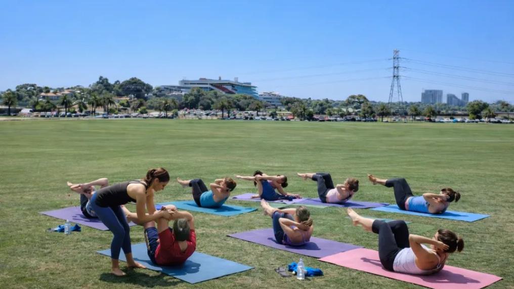 Outdoor group exercise class on the oval with people on mats.