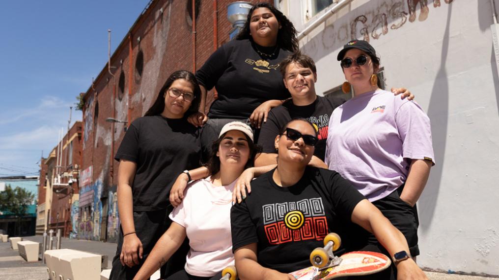 Smiling group of students in the sun wearing t-shirts with first nations graphics.