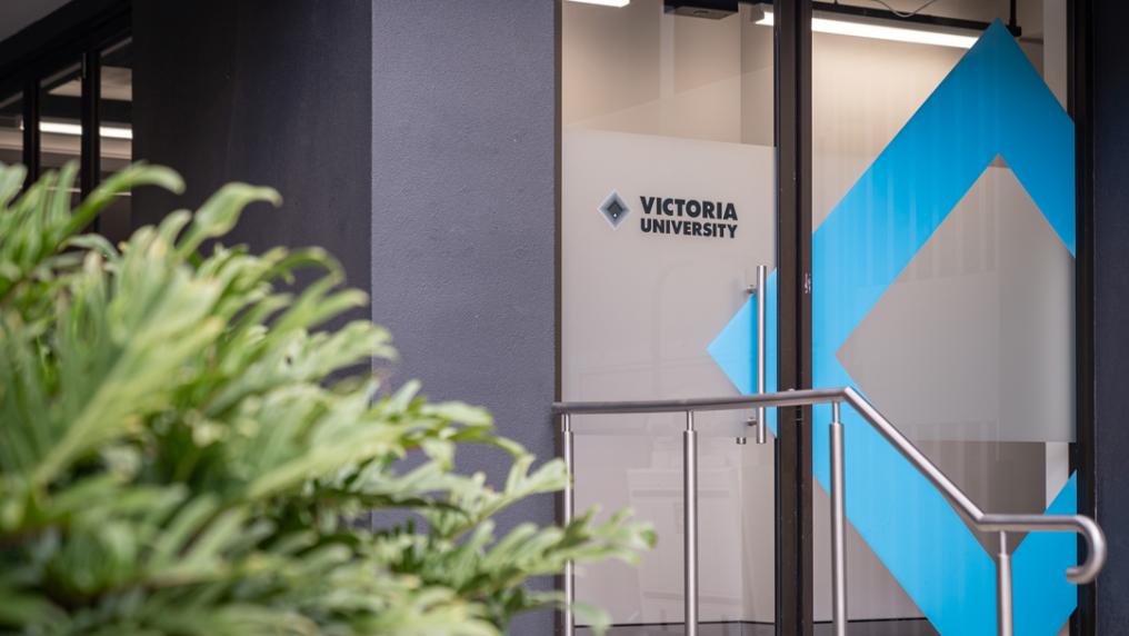 Exterior of glass door with Victoria University logo and handrail. 