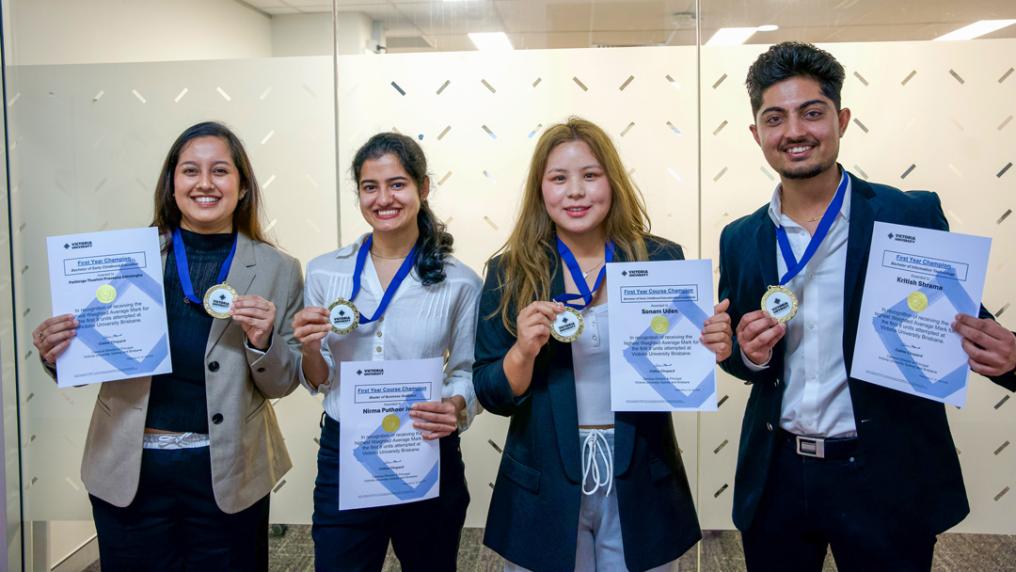 Four smiling students holding medals and certificates