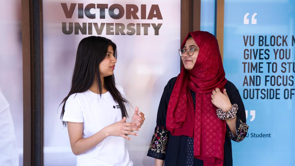 Student speaking to student support person, with Victoria University signage behind them.