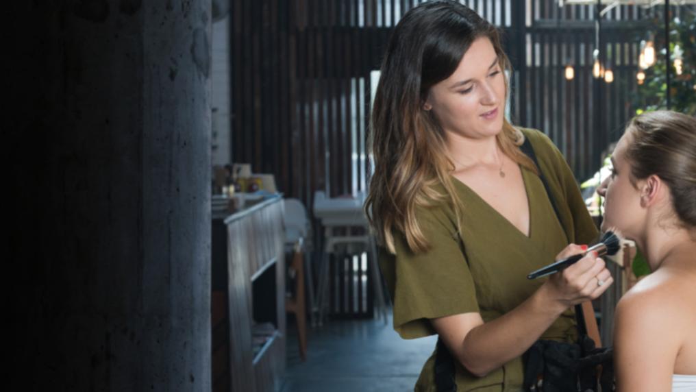 A young woman with professiongal make-up kit applies make up to another young woman