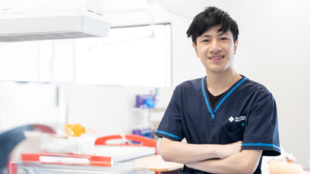 Young man in a Victoria University scrubs in a healthcare setting