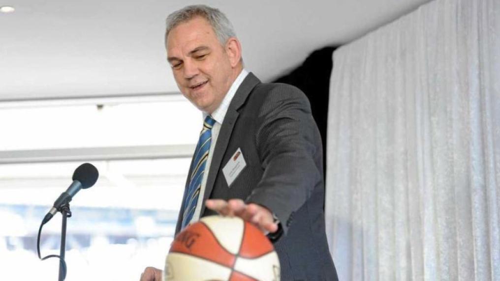 Man in suit holding a basketball at speaker's podium. 