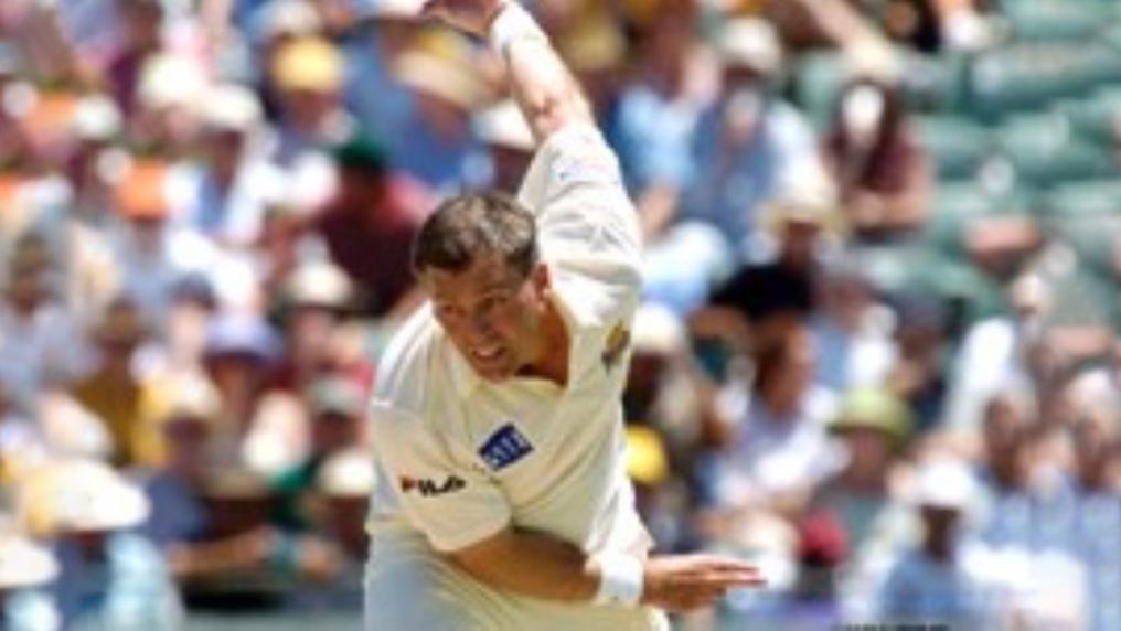 Male cricketer bowling in front of crowd.