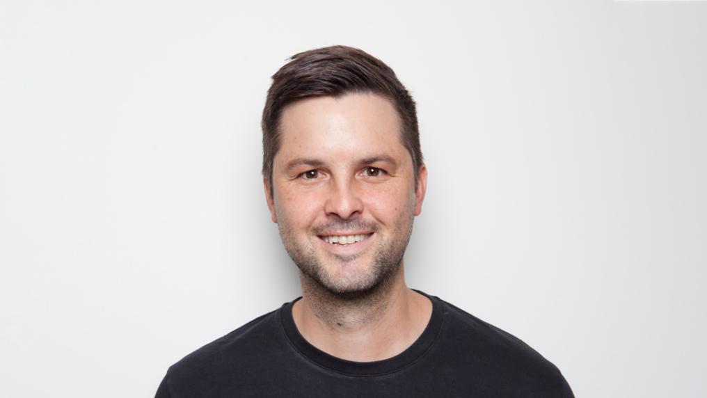 Smiling headshot of man in black t-shirt.  
