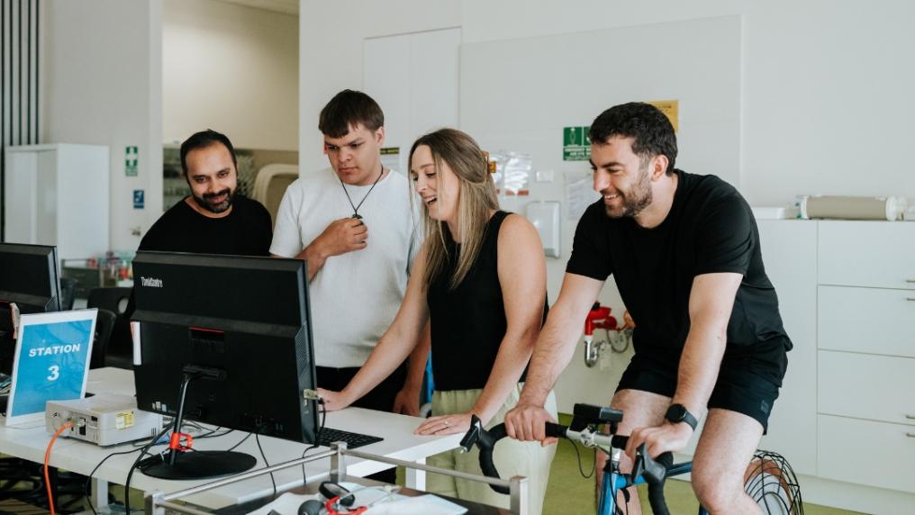 Exercise physiology students stand around computer and stationary bike