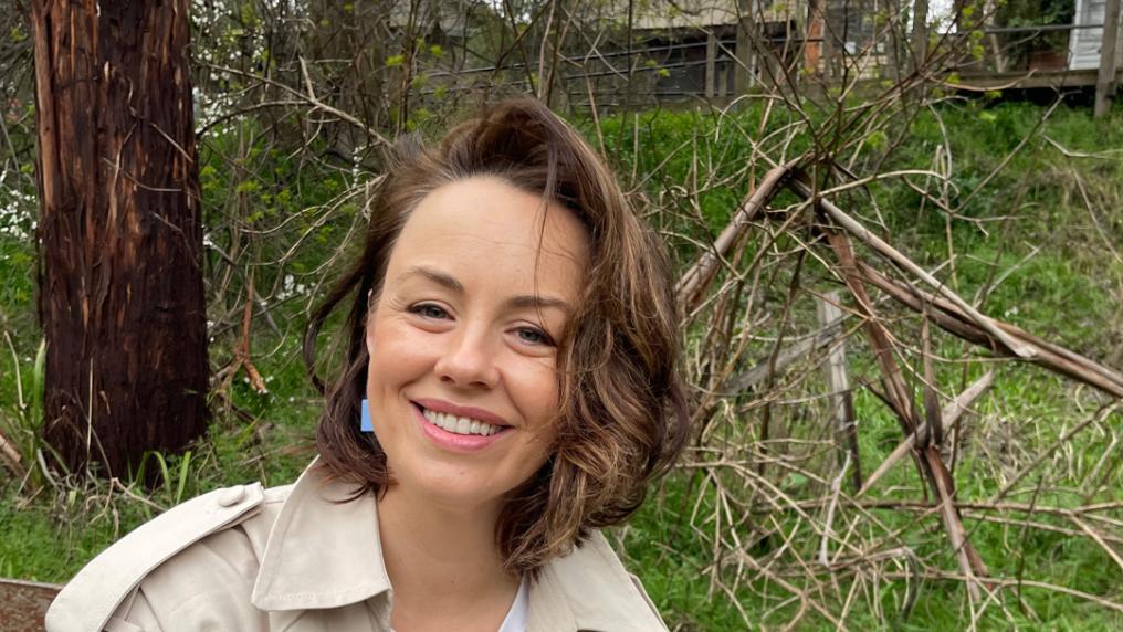 Smiling woman outdoors with trees and branches in background. 