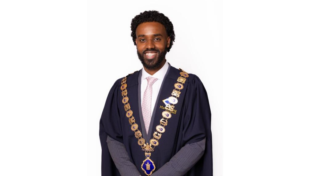 Smiling man in black formal gown and ceremonial gold chain.