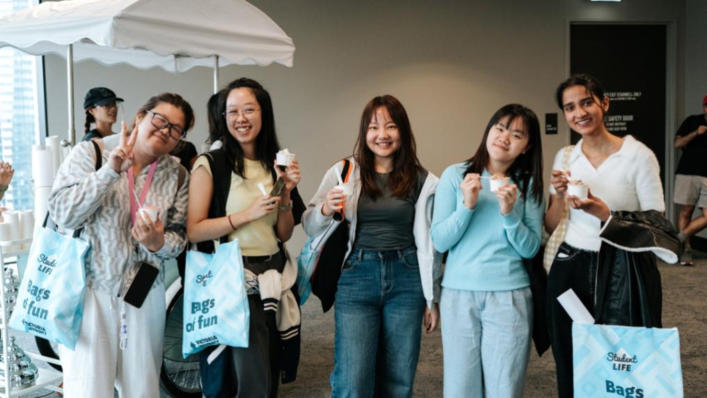 A group of students pose in front of an icecream cart with blue Victoria University tote bags