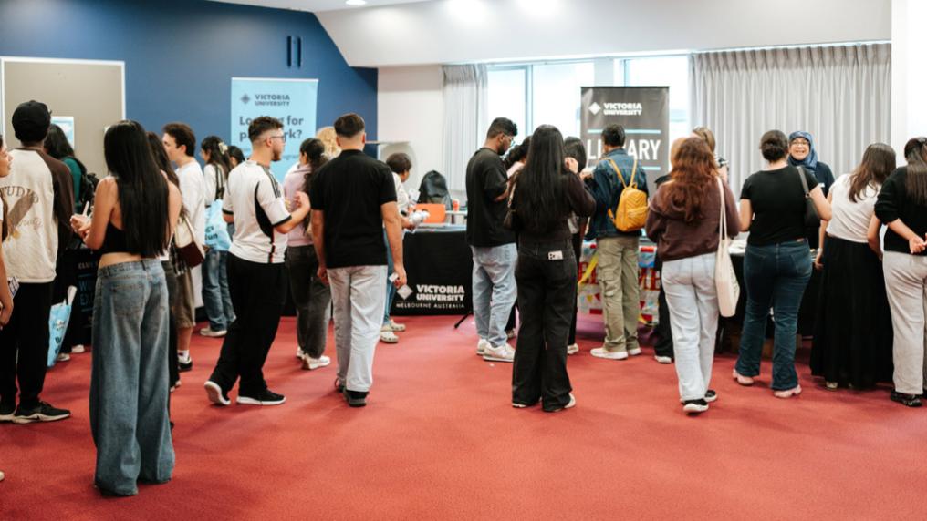 A large group of students mill around a room with Victoria Univerity signage and stalls