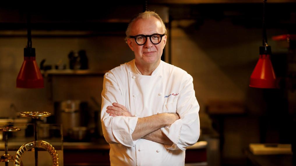 A middle aged man in a white chef jacket and horn-rimmed glasses in a country kitchen