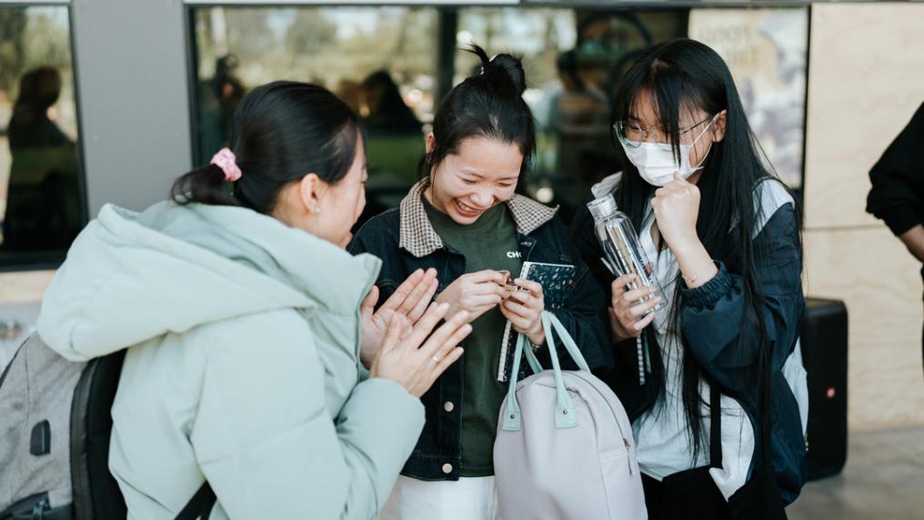 3 young women laughing and enjoying themselves outside a sleek glass building entrance