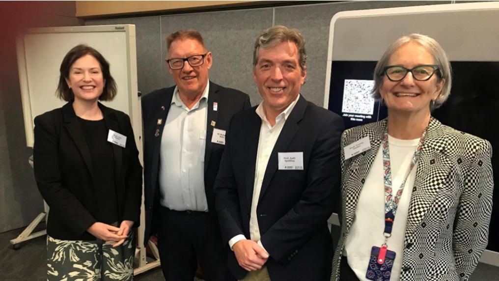 Four attendees standing together at a professional event wearing badges indoors.