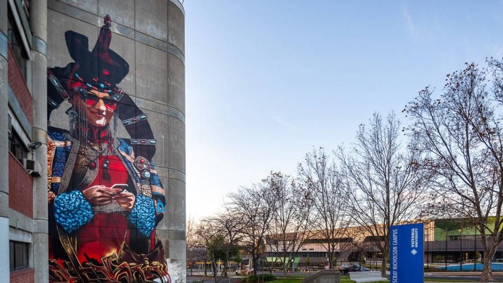 Colourful mural of a person on the side of a building with sky and trees to the side
