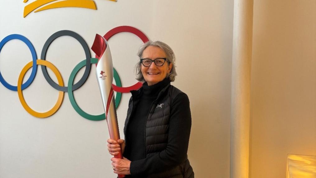 Individual holding a ceremonial torch beside a wall featuring the Olympic rings symbol.