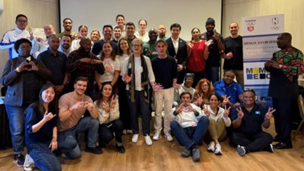 Large indoor group gathered on a wooden floor, arranged in rows for a team or event photo.