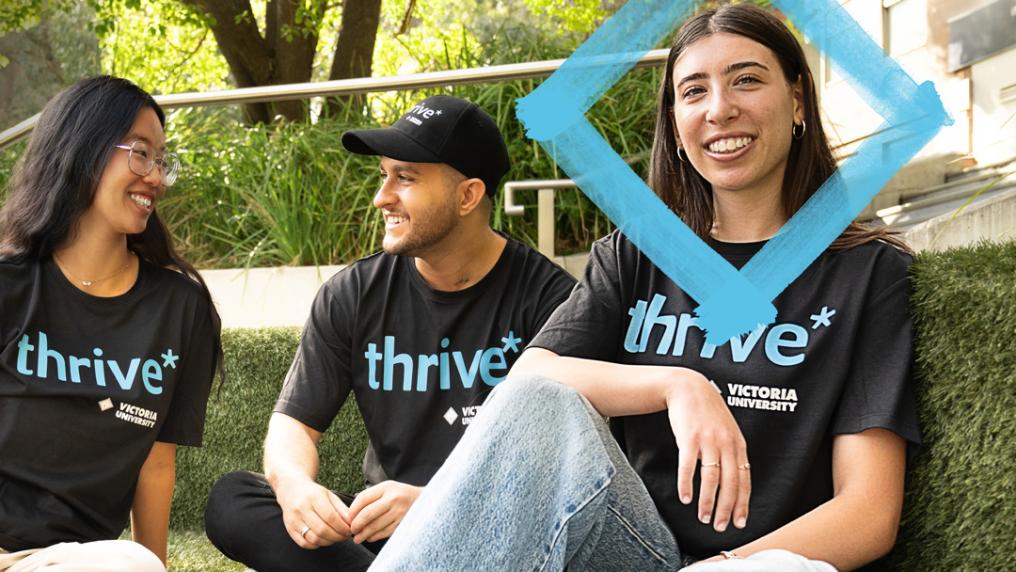 Three people are seated outside, smiling and chatting, wearing black t-shirts with 'Thrive' slogan.