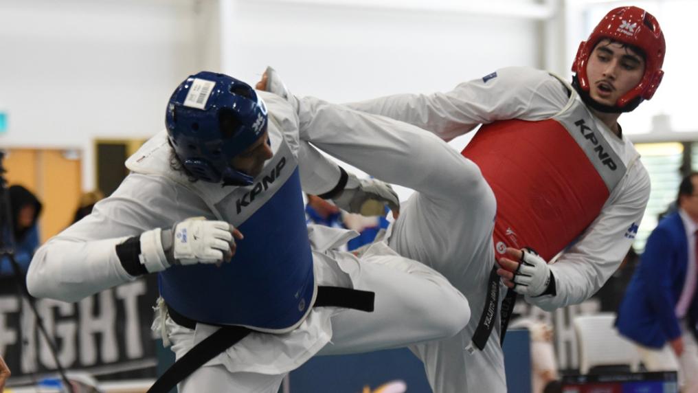 A taekowndo match mid-action with a red and blue uniforms