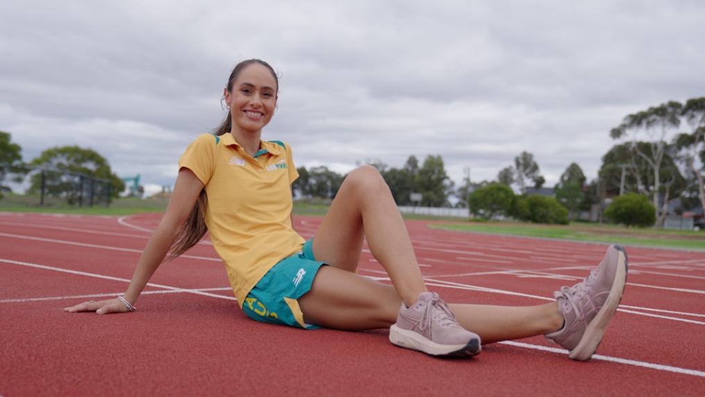 A young female athlete in Australian gold and green poses on a professional running track