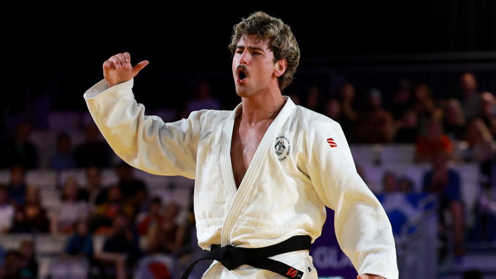 A young man in Judo uniform with black belt in front of a stadium crowd