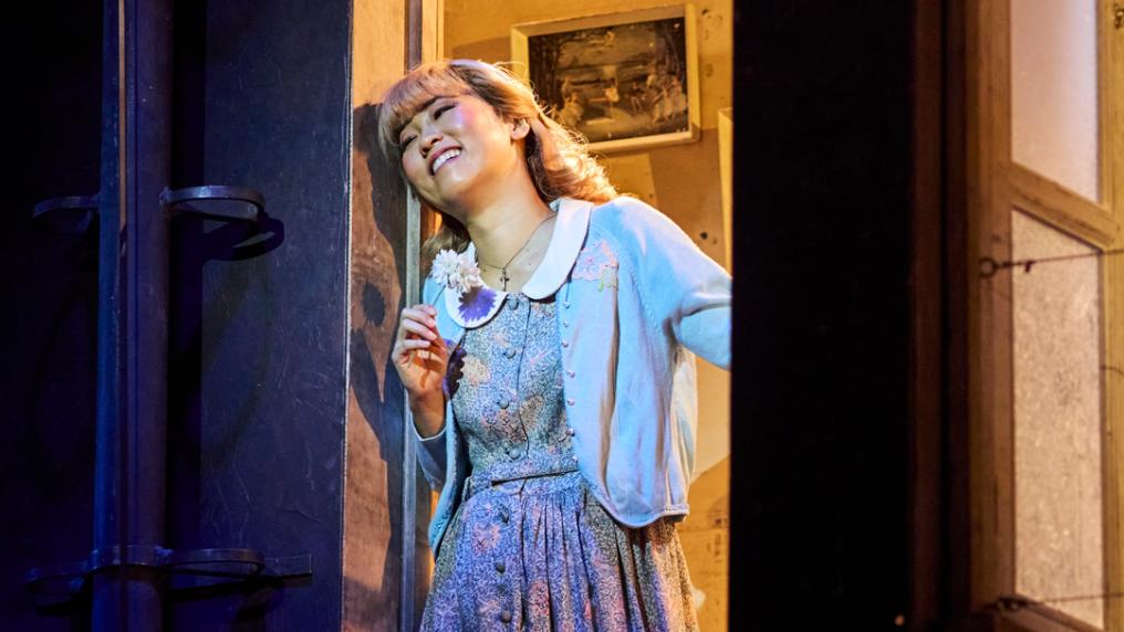 A young woman in 1940s costume at an open window of a stage set