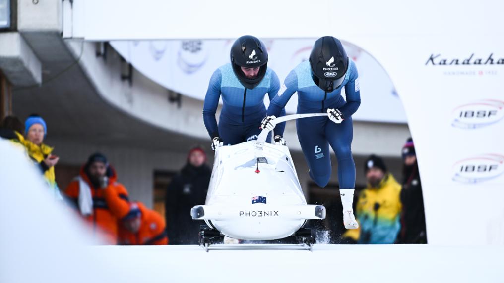 A two-person bobsleigh team taking off in full gear and helmets