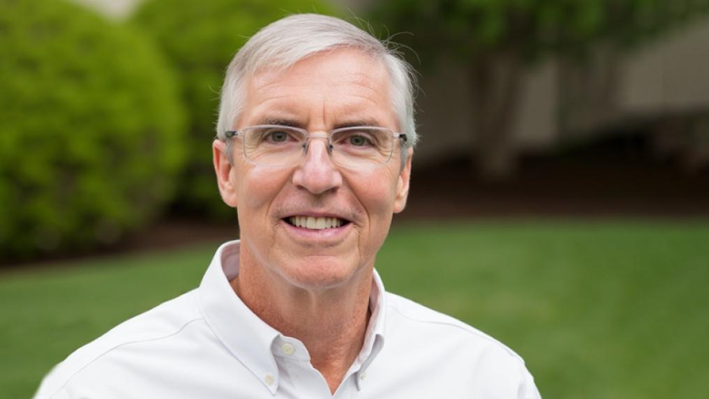 A man with grey hair and glasses poses in a well-tended lawn area