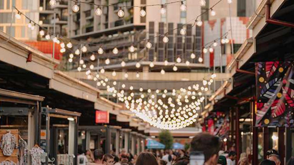 A busy city market strung with fairy lights and stall signs