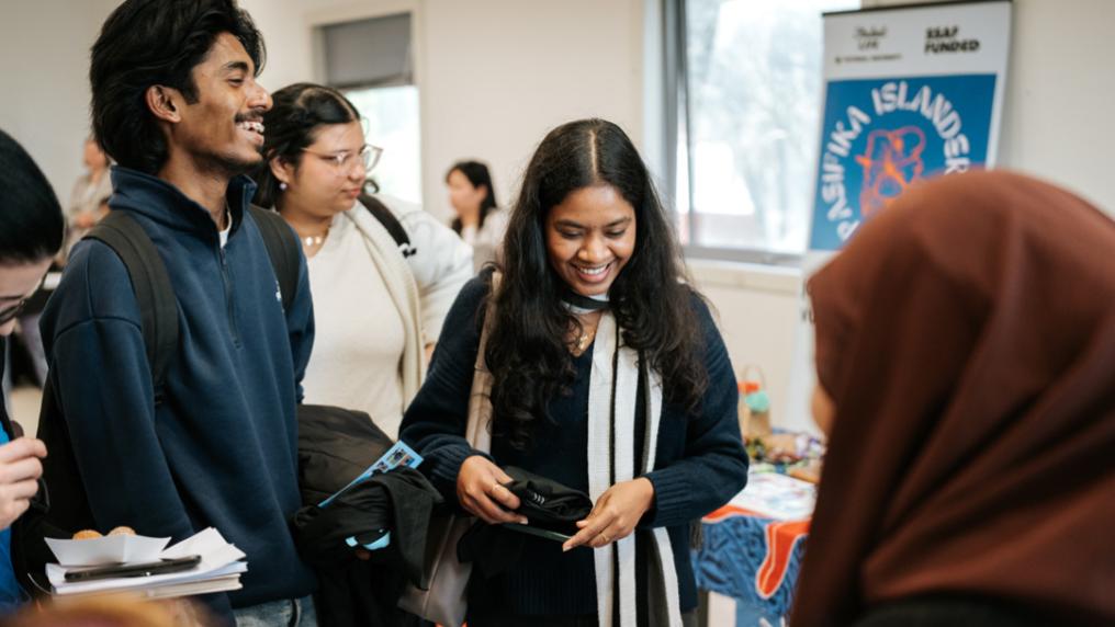 A multicultural group of students laugh and check out stalls at a social event