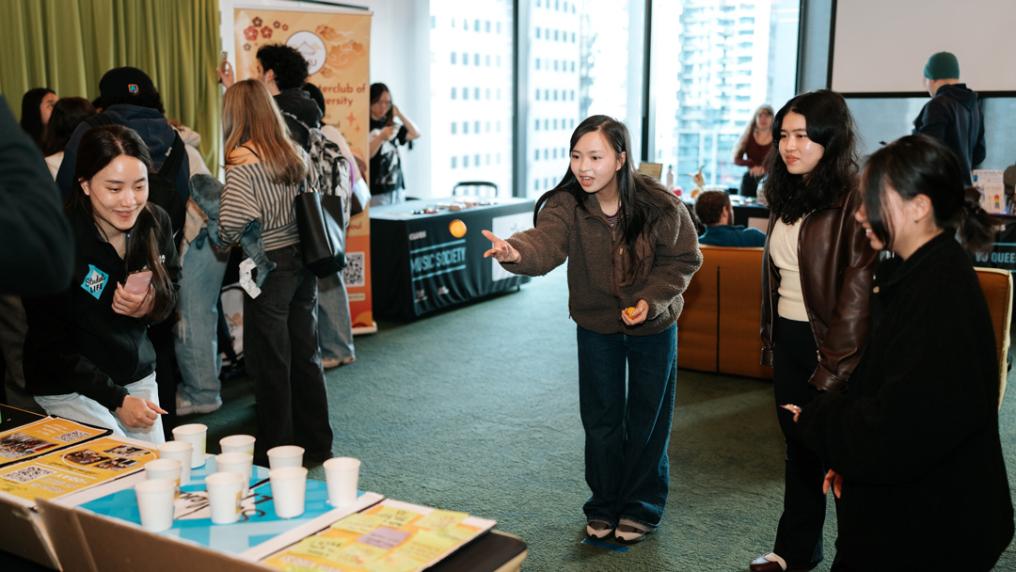 A group of students play a game of throwing balls into paper cups at a university event in a highrise building