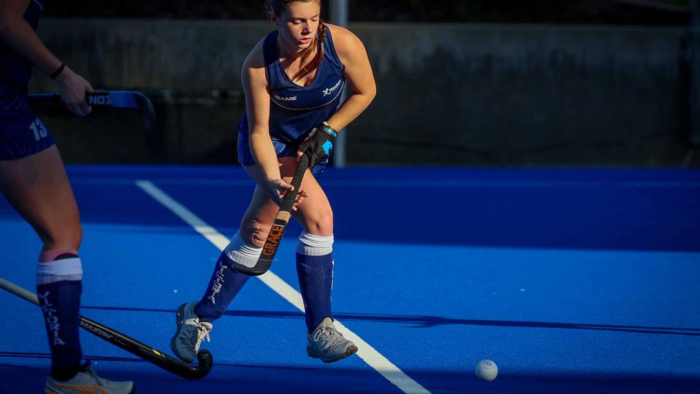 A young athletic woman in sport uniform plays a hockey match