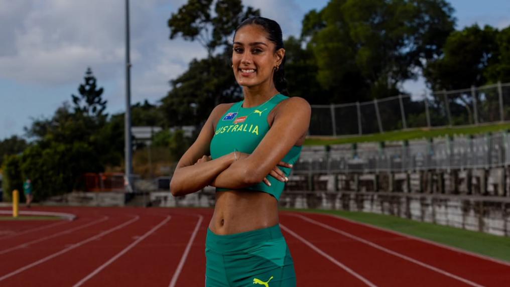 A young female athlete in Australian gold and green poses on a professional running track