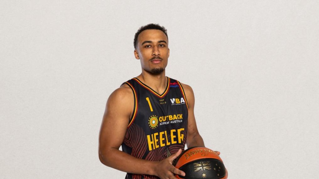 A young male athlete in sport uniform poses with a basketball