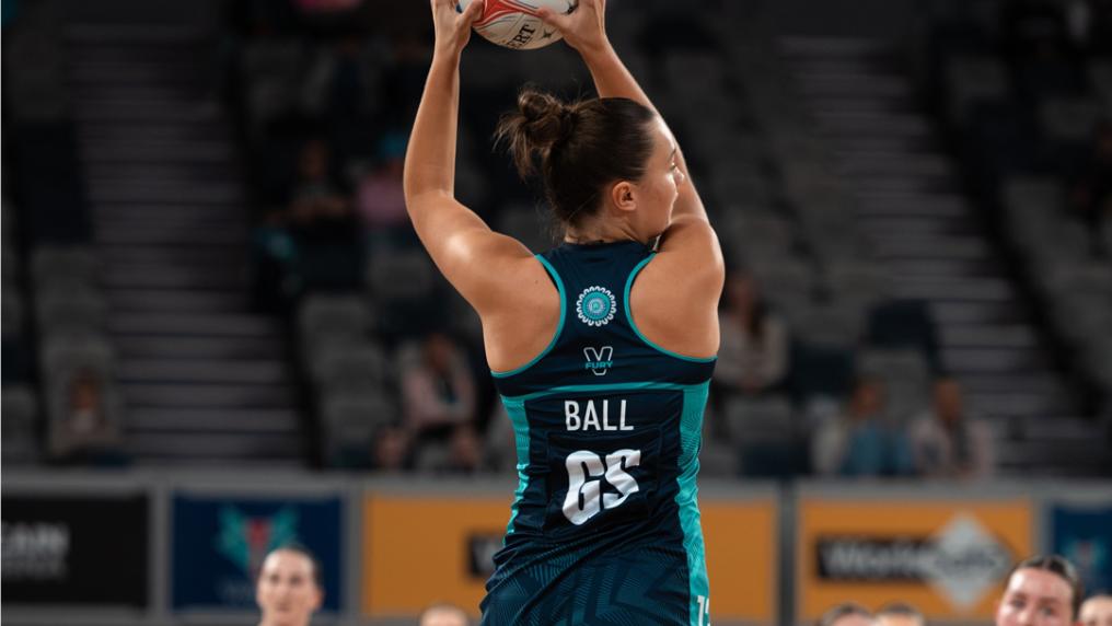 A young athletic woman in netball uniform leaps to catch a netball