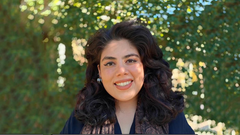 Woman outdoors smiles at camera with blurred background of trees and leaves