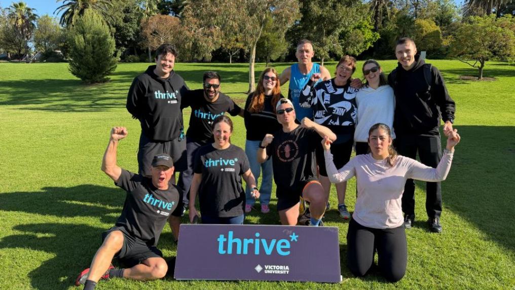 A group of runners posing in a park behind a sign that says thrive*. 