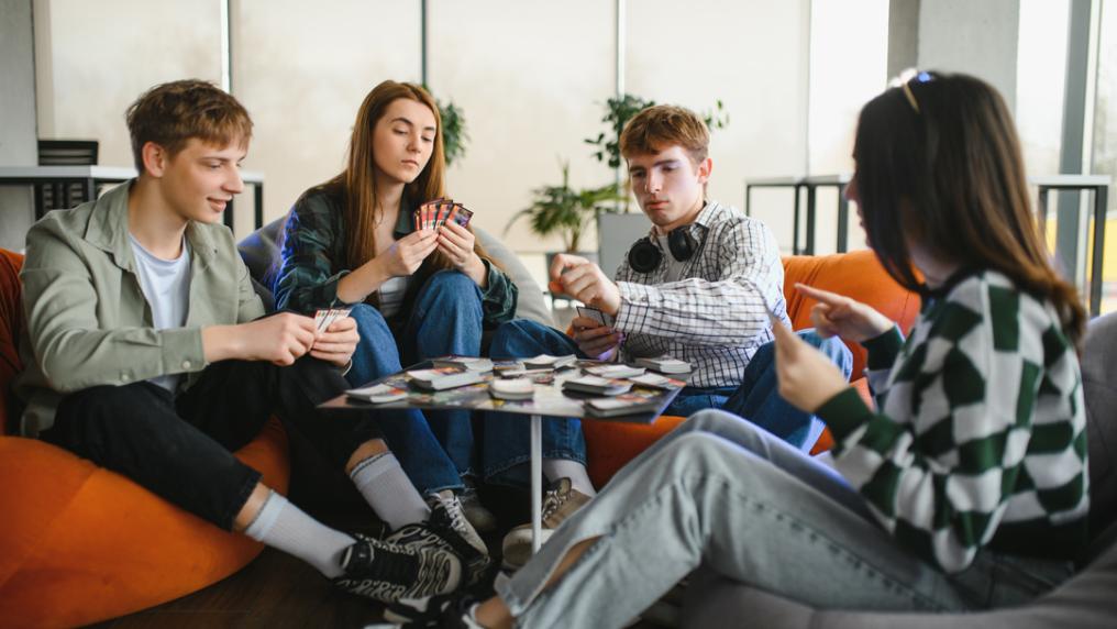 Friends sitting on bright beanbags playing card game in modern space