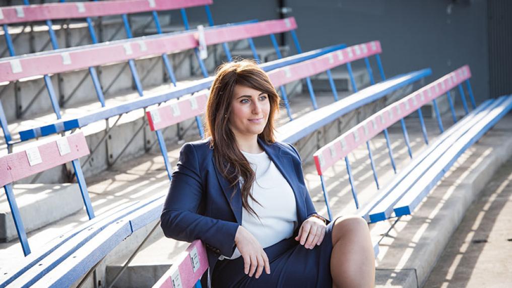 Catherine Dell’Aquila sitting in business attire outside on bleachers