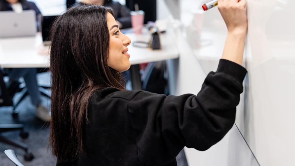 Young woman in a modern classroom writes on a whiteboard