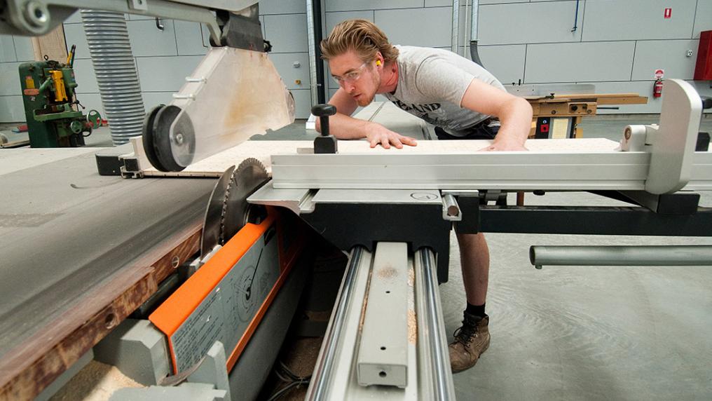 A young man in trade clothing operates large machinery