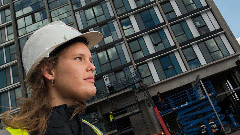 Emma Buis, engineering alumni, standing in front of skyscraper wearing construction hat.