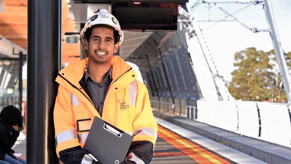 Kav Dassanayake in high vis clothing and wearing a helmet at a train station